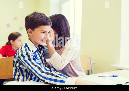 Sorridente schoolgirl whispering a classmate orecchio Foto Stock