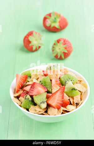 Cornflakes con fragola e kiwi fette nella ciotola bianco sul tavolo verde Foto Stock