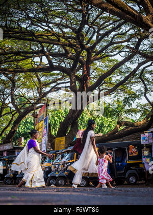 Le donne che passa una strada, un tuk-tuks in background, Bekal, Kerala, India Foto Stock