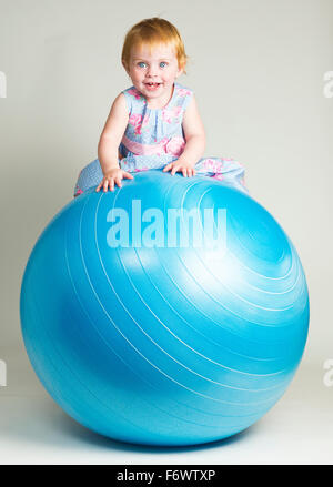 Un grazioso piccolo un anno vecchio ragazza seduta su di una sfera di equilibrio Foto Stock