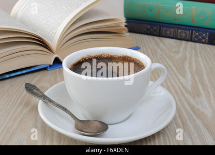 Una tazza di fragranti caffè nero sul tavolo contro lo sfondo di un libro aperto Foto Stock