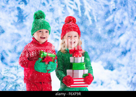 Bambina e ragazzo in rosso e verde Berretto lavorato a maglia Natale tenendo presente le caselle in winter park vigilia di Natale. Bambini a giocare all'aperto Foto Stock