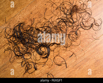 Ritagli di capelli su un pavimento parrucchieri. Un taglio womans marrone capelli sul pavimento di un salone di parrucchiere. Foto Stock