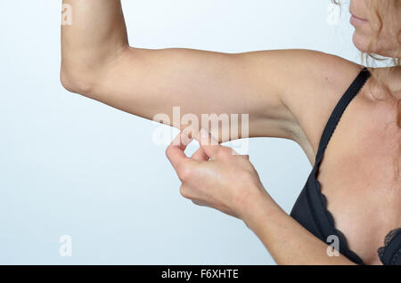 Donna di mezza età visualizzando la pelle allentata o flab a causa dell'invecchiamento sul suo braccio superiore stringere tra le dita, chiudere vie Foto Stock