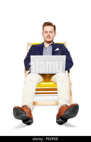 Bel uomo seduto su una sedia a sdraio e di lavoro sul computer. Isolato su sfondo bianco. Foto Stock