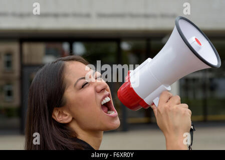 Arrabbiato giovane donna urlare su un megafono o bullhorn come lei partecipa a una manifestazione in strada o protesta di arieggiare il suo griev Foto Stock