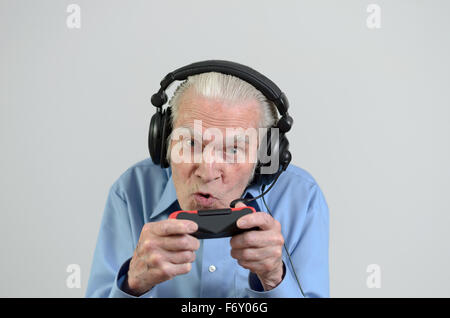 Funny uomo anziano o nonno utilizzando cuffie nero con le cuffie e il microfono durante la riproduzione di un video gioco su console Foto Stock