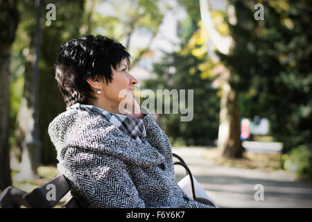 Bella donna middleaged con breve taglio di capelli scuri usando il dispositivo in posizione di parcheggio Foto Stock