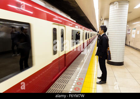 Un uomo giapponese in attesa in metropolitana per il passaggio di un treno Foto Stock