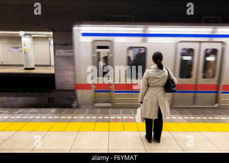 Una donna giapponese in attesa in metropolitana per il passaggio di un treno Foto Stock