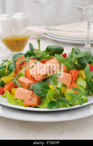 Insalata di verdure con fette di salmone, radici, foglie di rucola, pomodori e peperoni, condite con la salsa di senape con curry Foto Stock