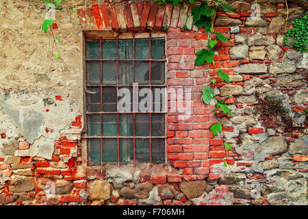 Frammento del vecchio abbandonato casa di mattoni con finestrino chiuso dietro sbarre di ferro nella piccola città italiana in Piemonte, Italia settentrionale. Foto Stock