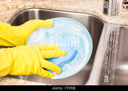 Una persona che bagna la cena piastre utilizzando detergente saponosa, una spugna e guanti di protezione e poi li risciacqui prima dell'essiccazione Foto Stock