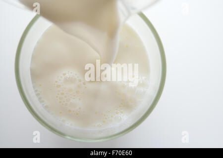 Il latte che viene versato in un bicchiere Foto Stock