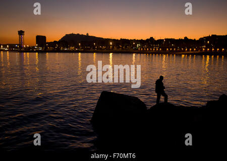 Un uomo pesca dal molo al tramonto a Barcellona il 19 novembre, 2015. Foto Stock
