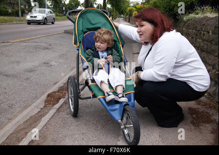 Madre accovacciato e chiacchierare al suo Figlio bambino seduto nel suo buggy, Foto Stock