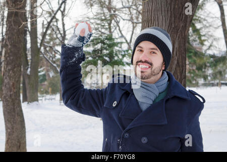 Giovane uomo di gettare una palla di neve in una coperta di neve park Foto Stock