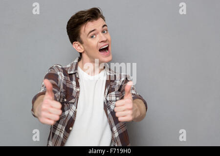 Gioioso allegro bello lieto felice giovane uomo in plaid shirt dando pollice in alto Foto Stock