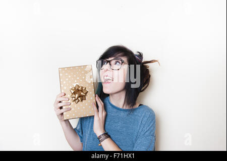 Piuttosto giovane donna allegra holding gold confezione regalo tra le mani Foto Stock