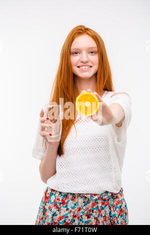 Allegro candida felici piuttosto redhead girl in top bianco e gonna floreale holding bicchiere vuoto e l'offerta di arance mature Foto Stock