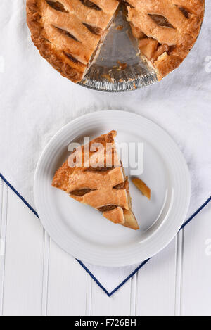 Vista aerea di una fetta di torta di mele su una piastra il resto della torta è nella parte superiore del telaio. Formato verticale su asciugamano bianco Foto Stock