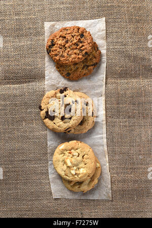 Angolo di alta vista di tre piccole pile di sfornato fresco holiday cookie su una striscia di carta pergamena su tela coperti da tavola. Foto Stock