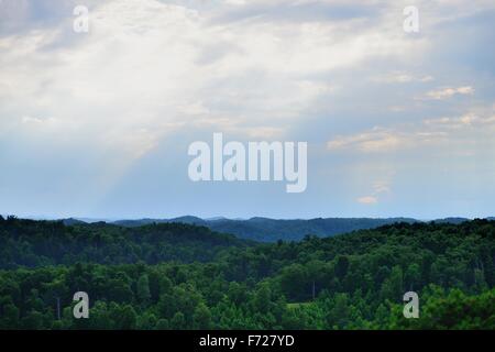 Un incredibile cielo di sera con i raggi di luce che risplende al di sopra di una foresta verde con un lago nel centro. Foto Stock