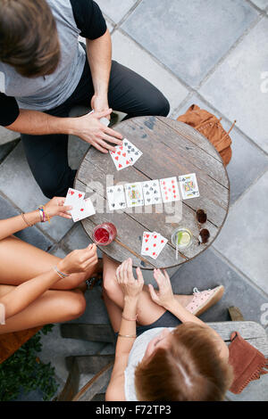 Tre giovani amici giocando a carte presso il cafe. Direttamente sopra il colpo di giovani uomini e donne sedute intorno ad un cafe' all'aperto e tabella Foto Stock