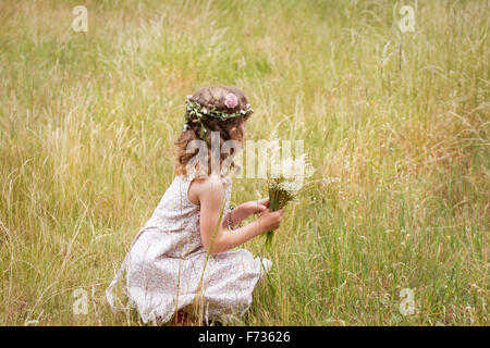 Ragazza giovane con fiori nei capelli picking fiori selvatici in un prato. Foto Stock