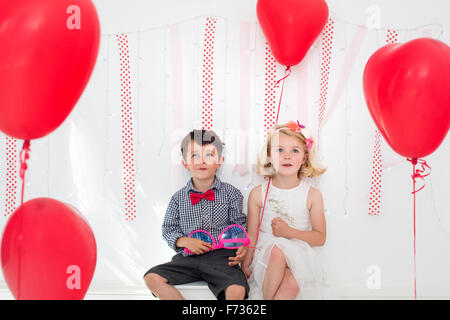 Ragazzo e ragazza in posa per una foto in un studio di fotografi, circondato da palloncini rossi. Foto Stock