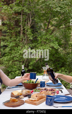 Tabella in un giardino con piastre e cibo, un uomo versando un bicchiere di vino. Foto Stock