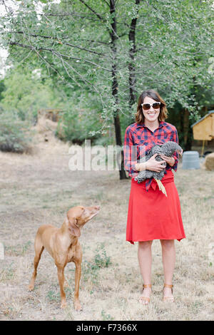 Ritratto di una donna sorridente tenendo una gallina grigio, un cane in piedi accanto a lei. Foto Stock