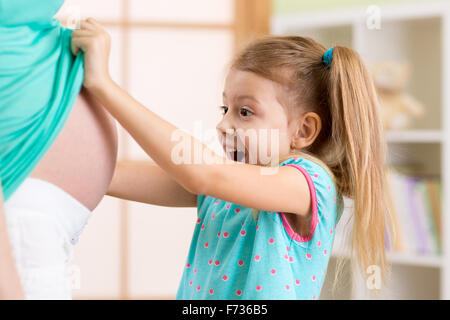 Bambino ragazza guardando la madre incinta pancia Foto Stock