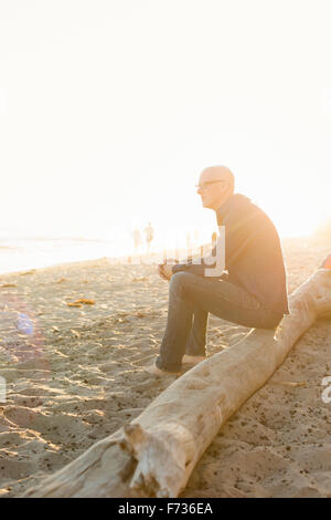 Bald uomo seduto su un log su di una spiaggia di sabbia. Foto Stock