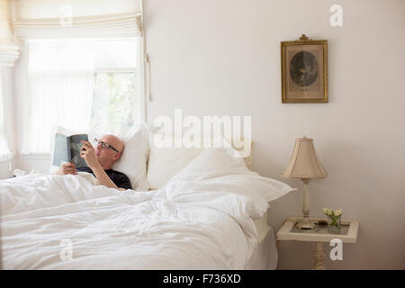 Uomo disteso in un letto con biancheria bianca, lettura. Foto Stock