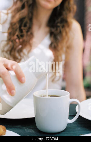 Donna versando il latte in una tazza di tè. Foto Stock