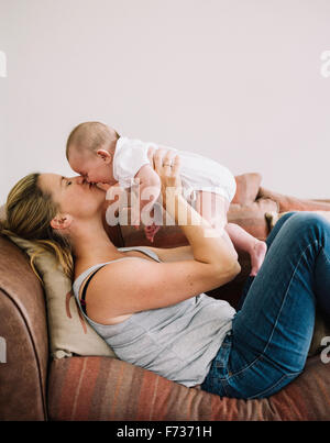 Una donna sdraiata su un divano a giocare con una bambina, bacio sulla guancia. Foto Stock