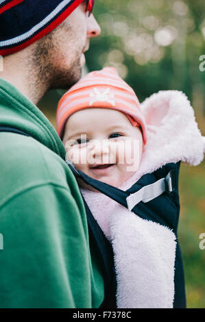 Un bambino in una imbracatura essendo portato da suo padre, all'aperto in inverno. Foto Stock