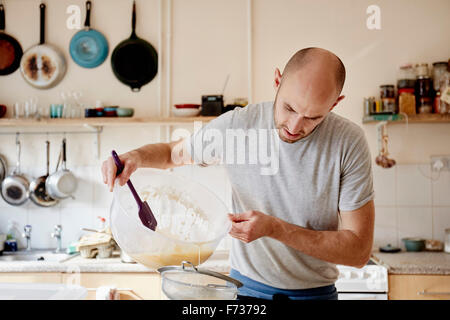 Un baker lavora in una cucina, versando un liquido in un recipiente attraverso un setaccio, rendendo l'impasto. Foto Stock