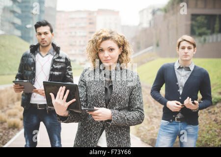 Multirazziale la gente di affari in posa all'aperto in città azienda dispositivi tecnologici come tablet e smartphone e computer - focus sull'imprenditrice lookin nella fotocamera - team, businees, il concetto di lavoro Foto Stock