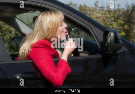 Donna automobilista applicando lip gloss utilizzando uno specchietto retrovisore Foto Stock