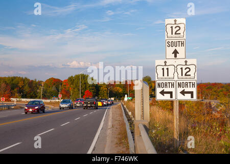 Road signs pointing to Highway 12 and Highway 11 on the side of a busy highway. Orillia, Ontario, Canada. Foto Stock