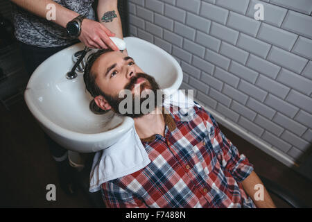 Parrucchiere il lavaggio dei capelli del giovane uomo attraente con la barba in camicia a scacchi nel salone di parrucchiere Foto Stock