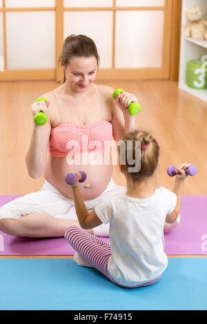 La donna incinta e il suo bambino più anziano facendo esercizi di fitness con manubri Foto Stock