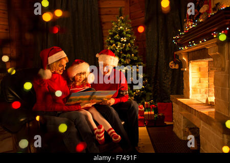 La famiglia felice la lettura di un libro di un albero di Natale in salotto accogliente in inverno Foto Stock