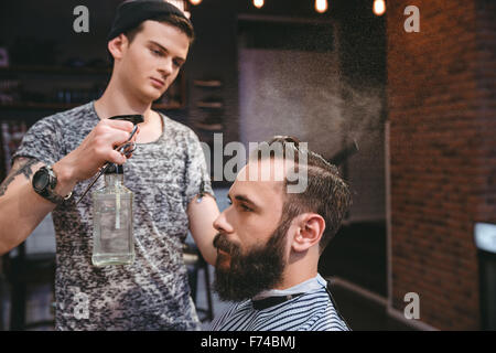 Bello concentrato parrucchiere spruzza con acqua dei capelli del cliente attraente con barba di Barber shop Foto Stock