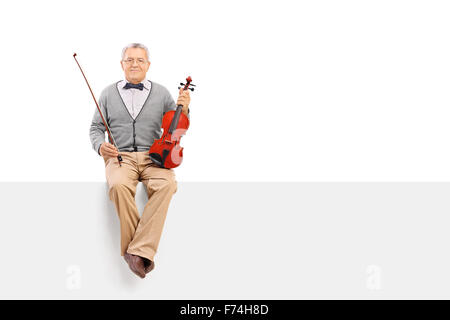 Il violinista maturo di trattenimento di un violino acustico e seduto su un cartello bianco isolato su sfondo bianco Foto Stock