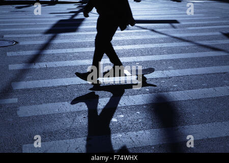 Blu notte ombre e silhouette di un irriconoscibile skateboarding maschio lungo una strada Foto Stock