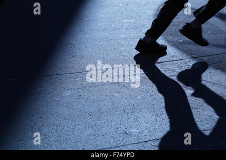 Blu notte ombre e silhouette di un irriconoscibile gioventù maschile di gambe in esecuzione al di fuori del frame giù per una strada di città Foto Stock