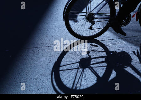 Blu notte ombre e silhouette di un irriconoscibile uomo ciclismo lontano dal telaio giù per una strada di città Foto Stock